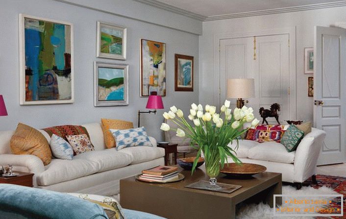 Soggiorno universale in stile eclettico. Una stanza accogliente crea molti cuscini e quadri astratti e luminosi che adornano il muro sopra il divano.