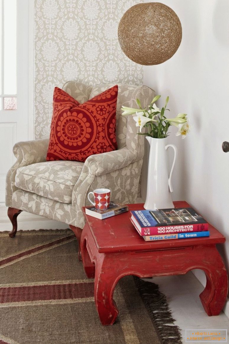 Angolo di lettura; tavolo da oppio e poltroncina pallida con cuscini a dispersione fantasia contro il muro tappezzato