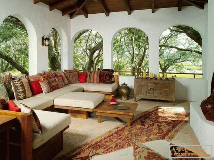 La veranda della casa di campagna è decorata secondo lo stile mediterraneo. Una caratteristica interessante è l'arredamento con un sacco di cuscini colorati.