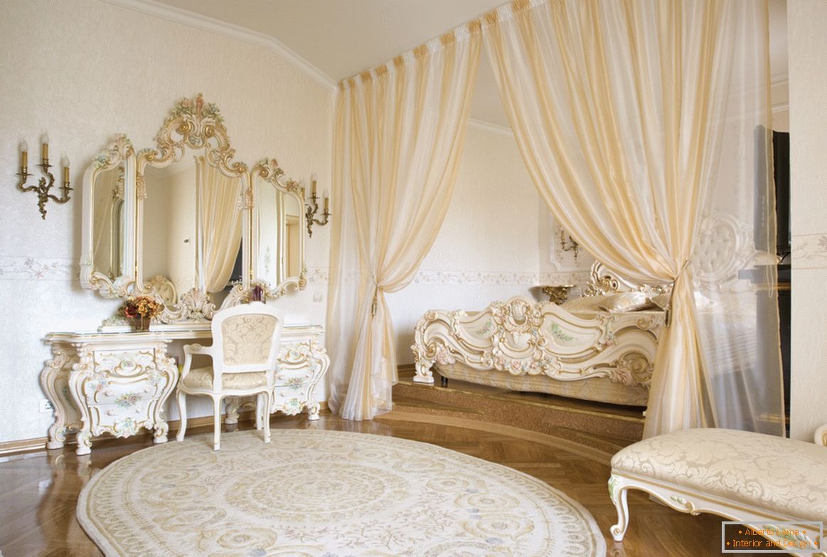 Specchi per cornici e elementi decorativi di mobili sono realizzati in uno stile con l'uso dell'oro. Per risparmiare spazio, il letto è nascosto in una nicchia incorniciata da tende.