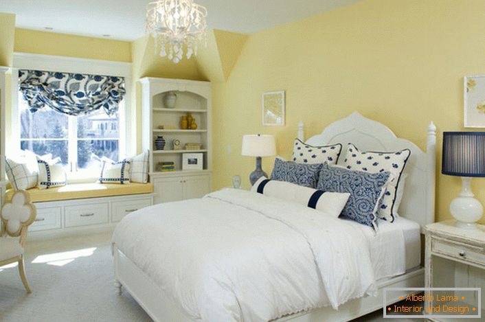 Il colore giallo sbiadito della finitura si armonizza con gli elementi bianchi e blu della decorazione. Una combinazione insolita è una soluzione audace per una camera da letto in stile country.