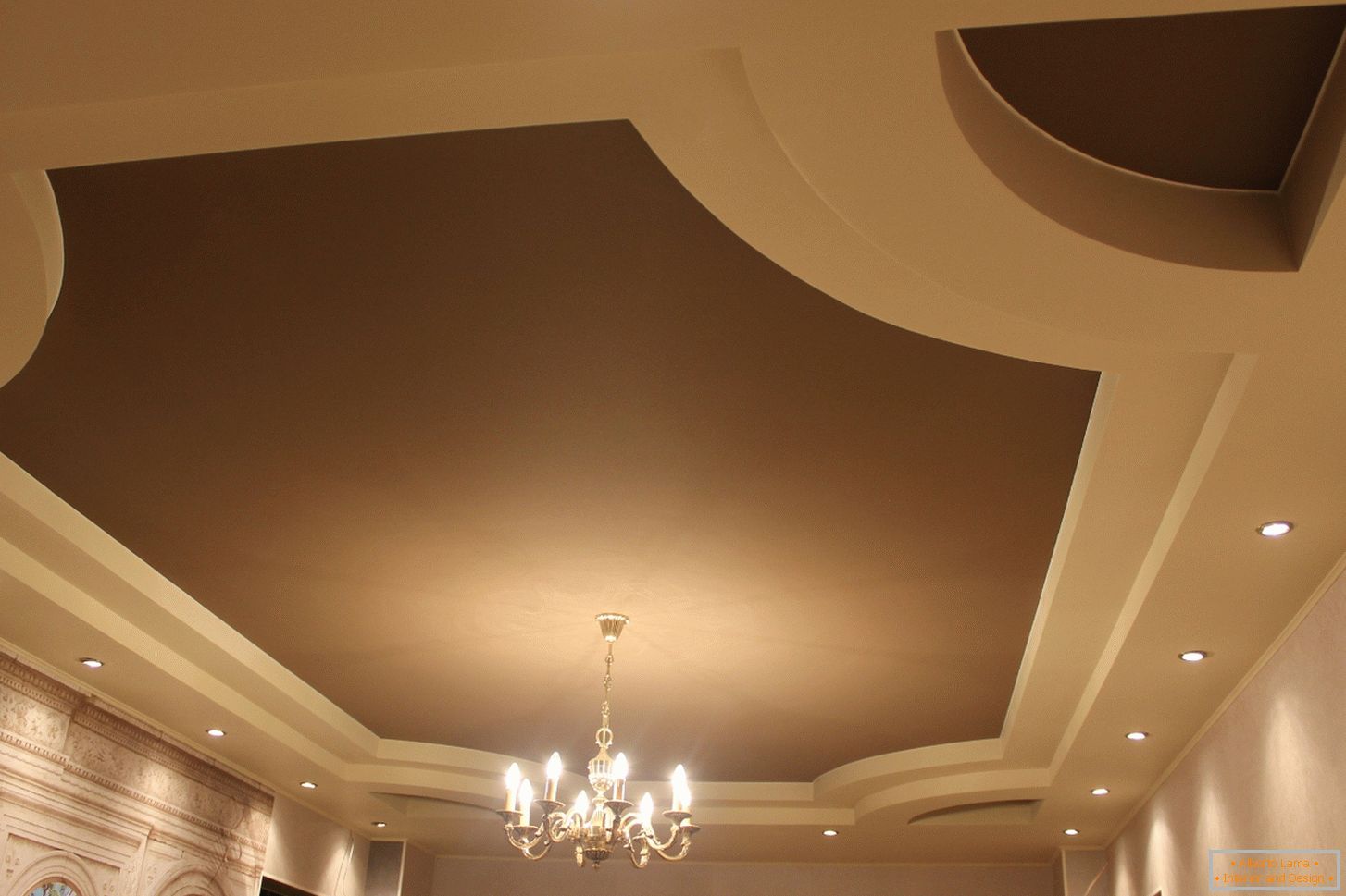 Soffitti in PVC elastico opaco per una camera per gli ospiti in una casa di campagna. La costruzione a più livelli dei soffitti sembra interessante nei colori beige chiaro e marrone scuro.