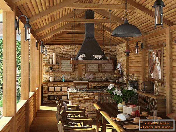 Una piccola cucina con barbecue sulla veranda di una casa di campagna. Lo stile country è evidenziato, prima di tutto, dalla decorazione delle pareti e del soffitto con una cornice di legno.