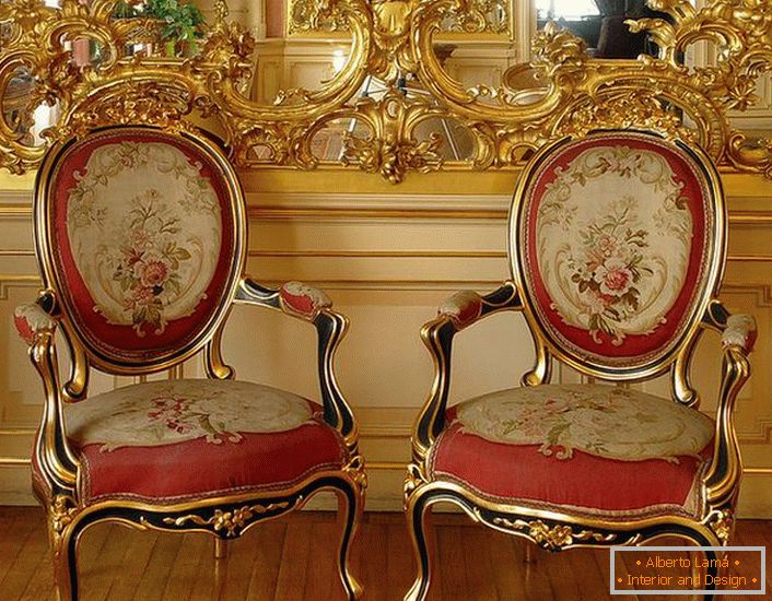 Stucco traforato di colore dorato sullo specchio e sedie con tappezzeria rossa morbida - rappresentanti luminosi dello stile barocco.