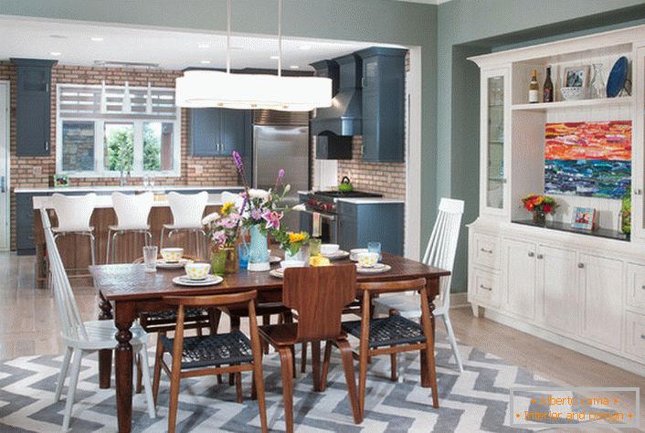Una grande cucina in stile eclettico è divisa in una zona di lavoro e sala da pranzo. La mobilia di colore bianco è unita a elementi di un interno di colore marrone scuro.
