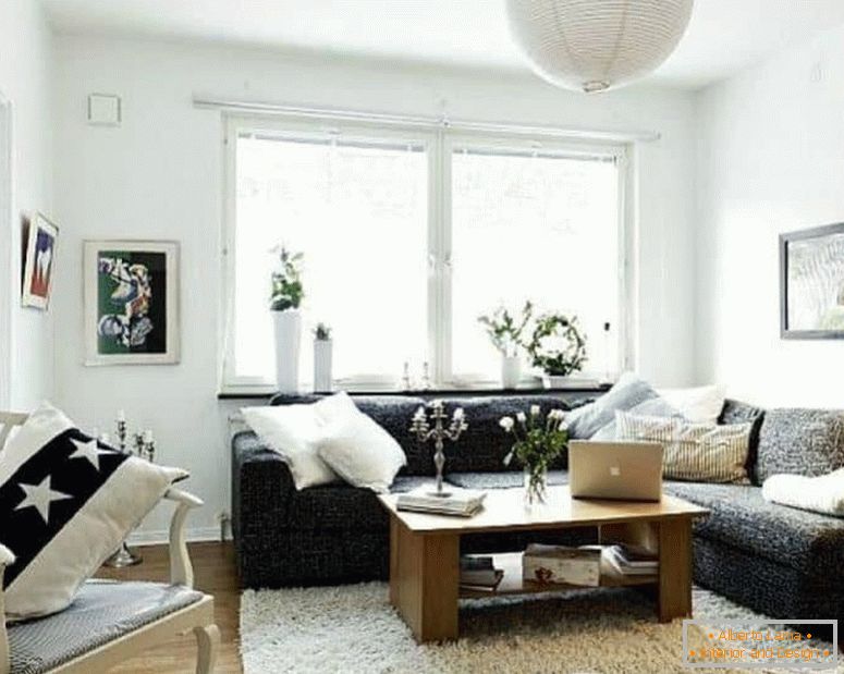 Un piccolo soggiorno in bianco con un divano angolare scuro e una finestra
