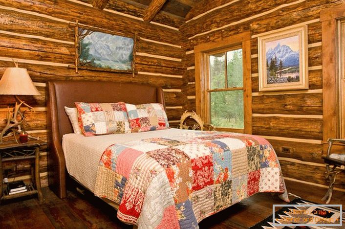 Una camera da letto in stile rustico in un capanno da caccia. Decorazione degna di nota delle pareti con l'aiuto di una casa di tronchi. 