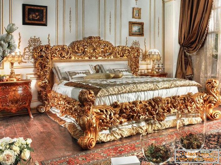 Un letto lussuoso è realizzato secondo le migliori tradizioni dello stile Impero. Spalli massicci di un letto di legno intagliato di nobile colore dorato si stagliano sullo sfondo di altri dettagli interni.
