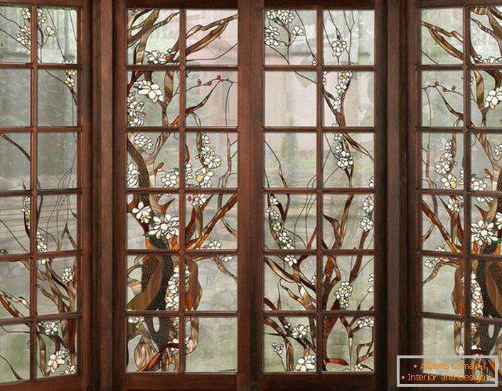 Le finestre nella cornice di legno scuro sono decorate con vetri colorati. Figura non complicata adatta per l'interior design in stile country o moderno.