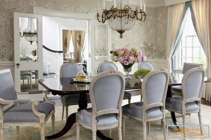 La sala da pranzo in stile neoclassico è decorata nei colori blu pallido e grigio chiaro. La carta da parati a fiori appare delicatamente in combinazione con alti zoccoli bianchi.