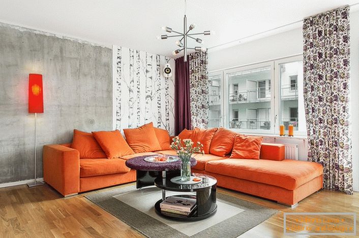 Lo stile scandinavo è inerente all'uso di colori caldi nel design degli interni. Morbido divano arancione guarda in modo organico sullo sfondo delle pareti di una tonalità grigio-freddo.