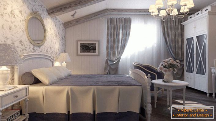 La camera da letto in stile country è realizzata in tenui toni blu. Il muro in testa al letto è ricoperto da carta da parati con motivi floreali.