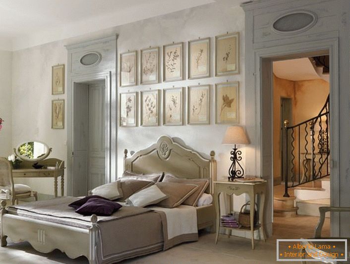 In conformità con le tradizioni dello stile francese per la camera da letto è stata selezionata la laconica luce dei mobili in legno. Un dettaglio interessante è un collage di immagini sopra la testa del letto.